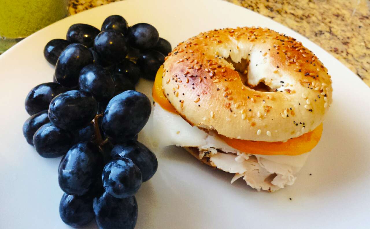 Turkey, swiss and tomatoes on a toasted bagel with grapes and a green